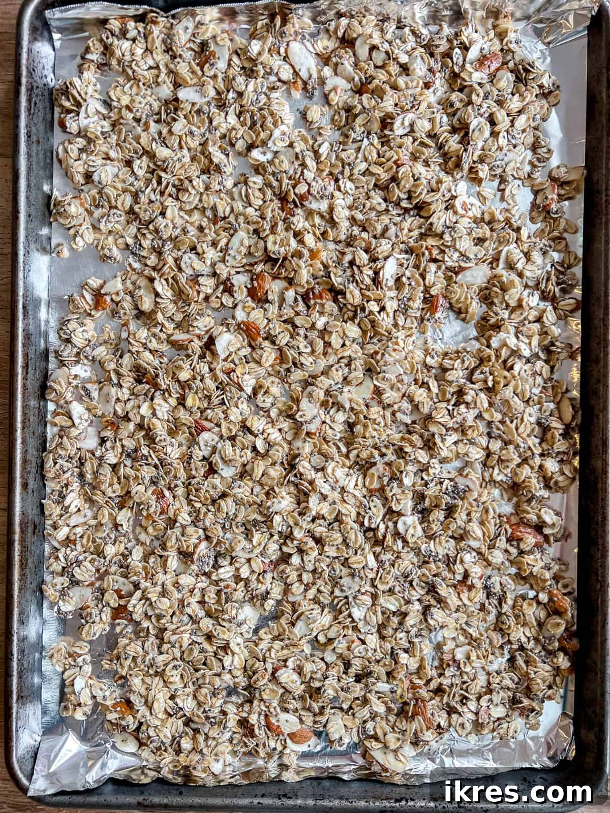 Granola with almonds and chia seeds spread on a baking sheet before baking.