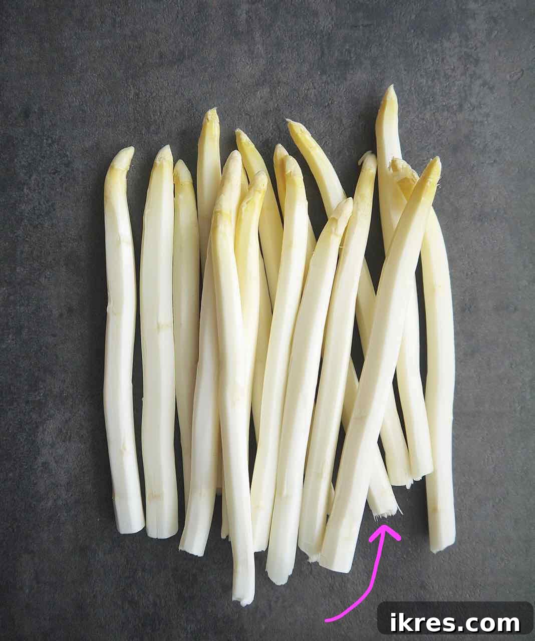 Spring White Asparagus with Provençal Citrus Mustard Dressing 6 Close-up of the bottom end of a white asparagus spear, with a red arrow pointing to a stringy, fibrous part that needs to be removed before cooking. This illustrates the 'snap test' and the importance of thorough peeling.