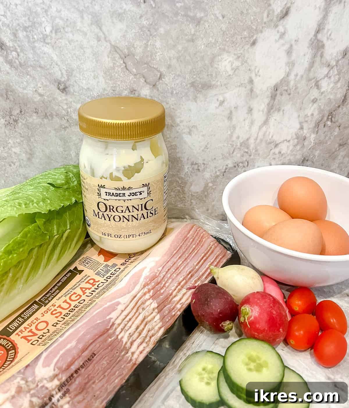 A selection of fresh ingredients including hard-boiled eggs, mayonnaise, lettuce, dill, radishes, tomatoes, and cucumbers.