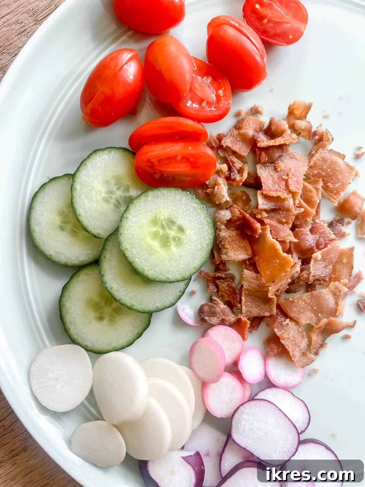 Assortment of fresh toppings for egg salad wraps including sliced radishes, cucumbers, and tomatoes, alongside crispy bacon.