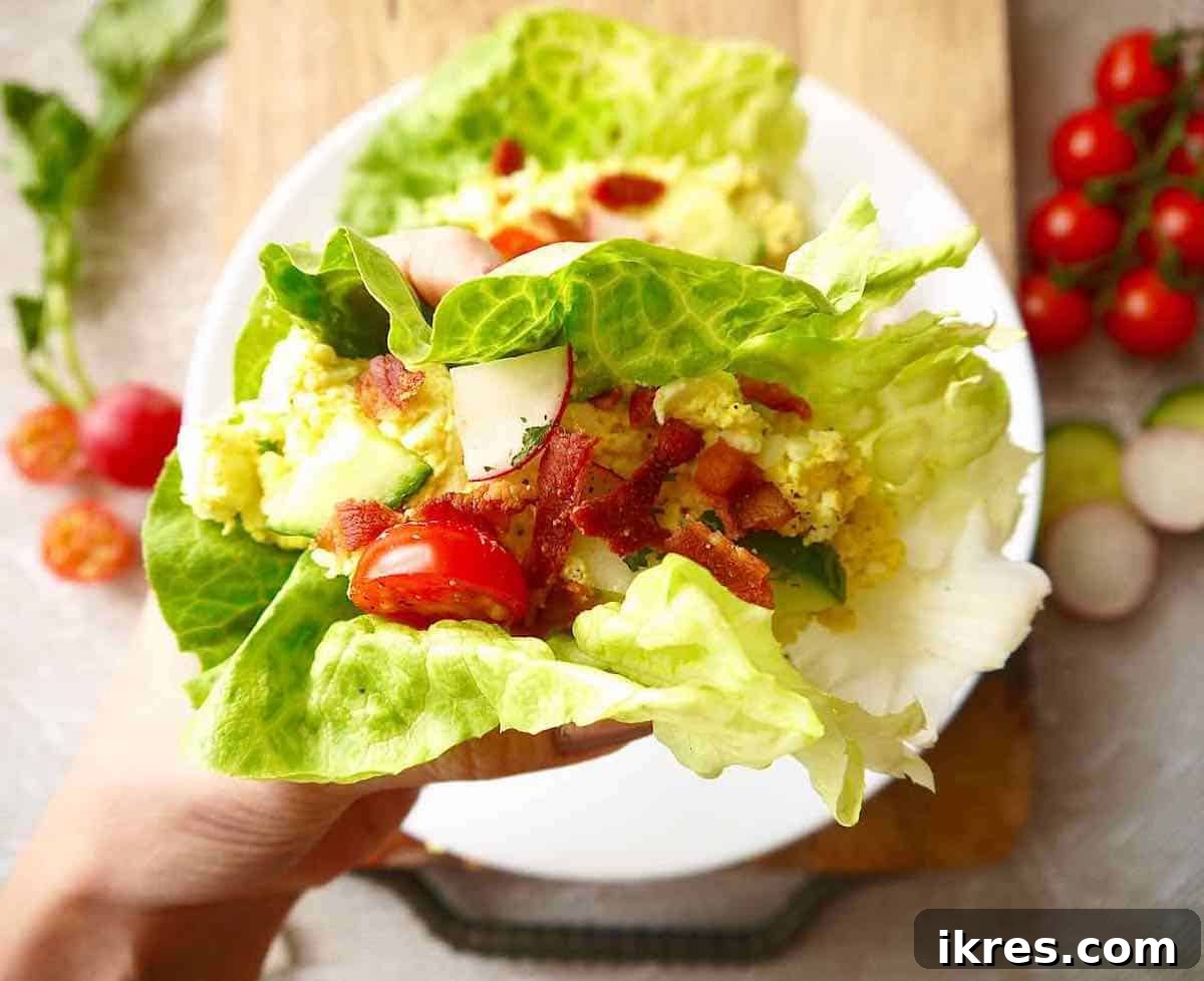 A hand holding an assembled egg salad lettuce wrap, showcasing the fresh toppings.