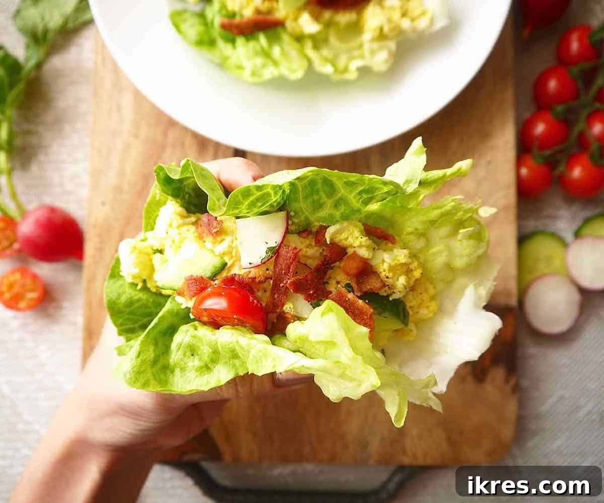 A person's hands delicately holding a freshly made egg salad lettuce wrap, ready to be eaten.
