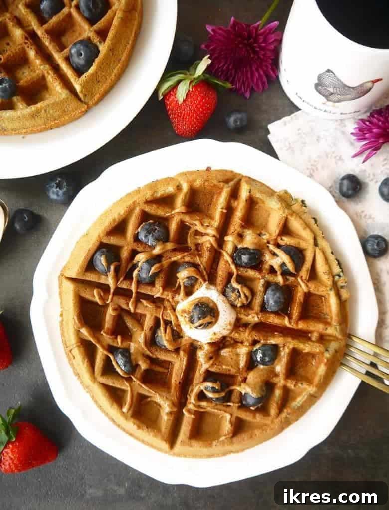 Close-up of fluffy Paleo gluten-free mashed blueberry waffles with blue flecks inside, stacked on a white plate, ready to be topped.