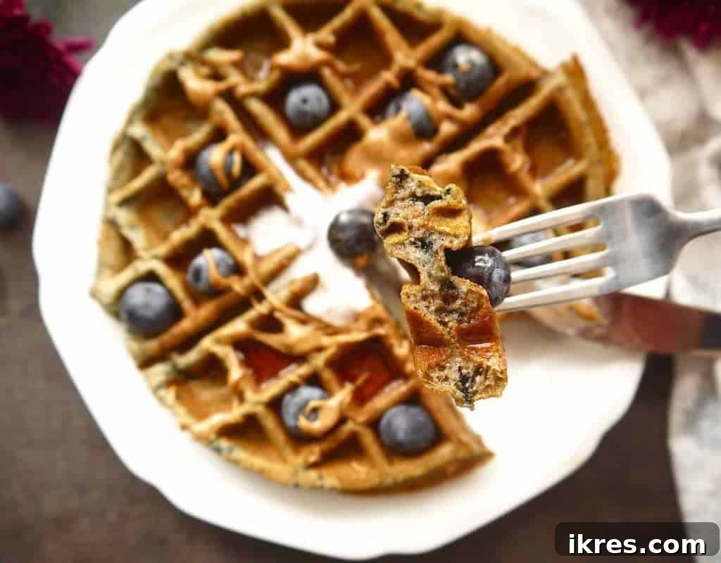Three golden brown Paleo gluten-free mashed blueberry waffles artfully arranged on a plate, garnished with fresh blueberries.