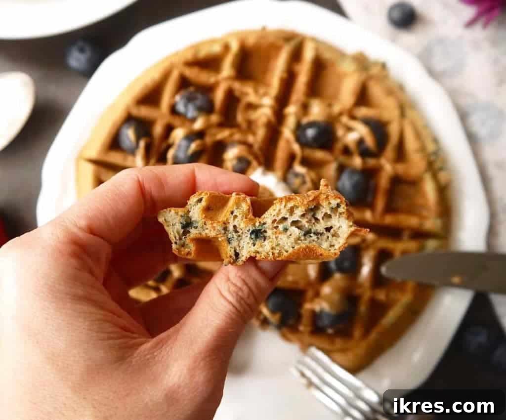 A beautifully presented Paleo gluten-free mashed blueberry waffle, topped with almond butter, maple syrup, and fresh blueberries.