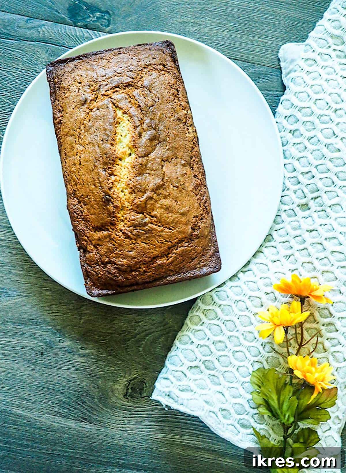 Perfectly Easy Bread Maker Banana Bread 4 A golden-brown, perfectly baked loaf of bread machine banana bread resting on a simple white plate, showcasing its moist texture.