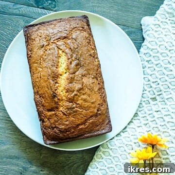Perfectly Easy Bread Maker Banana Bread 6 A freshly baked loaf of bread machine banana bread on a white plate, showcasing its golden crust and delicious appeal.