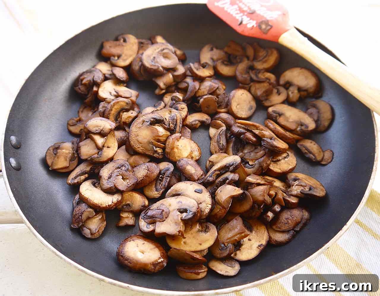 Sliced baby bella mushrooms browning in a pan, developing rich flavor.