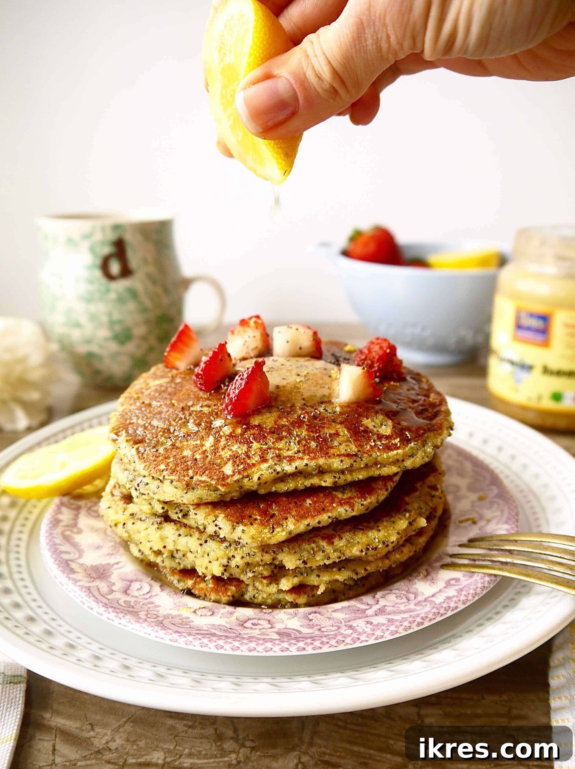 Paleo Zesty Lemon Poppy Seed Pancakes 2 Stacked lemon poppyseed pancakes garnished with fresh strawberries and a drizzle of maple syrup.