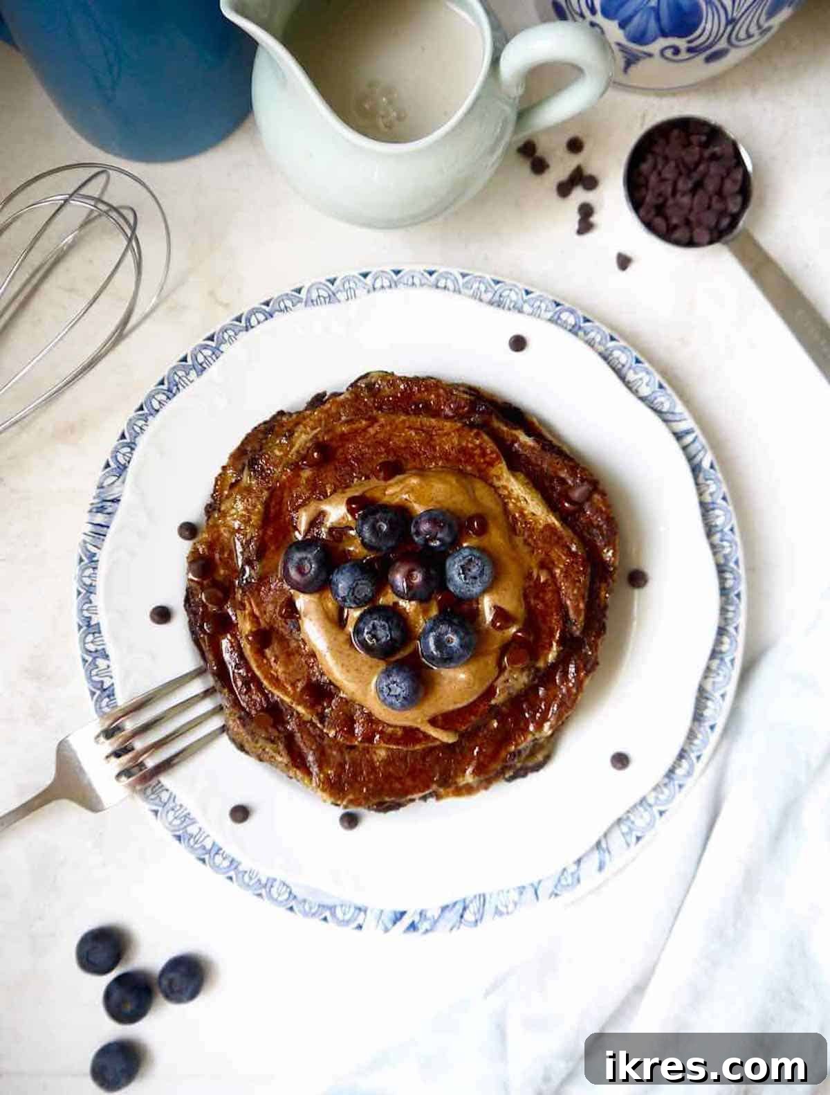 Healthy banana pancakes recipe on a plate with blueberries, and almond butter on top for serving inspiration.