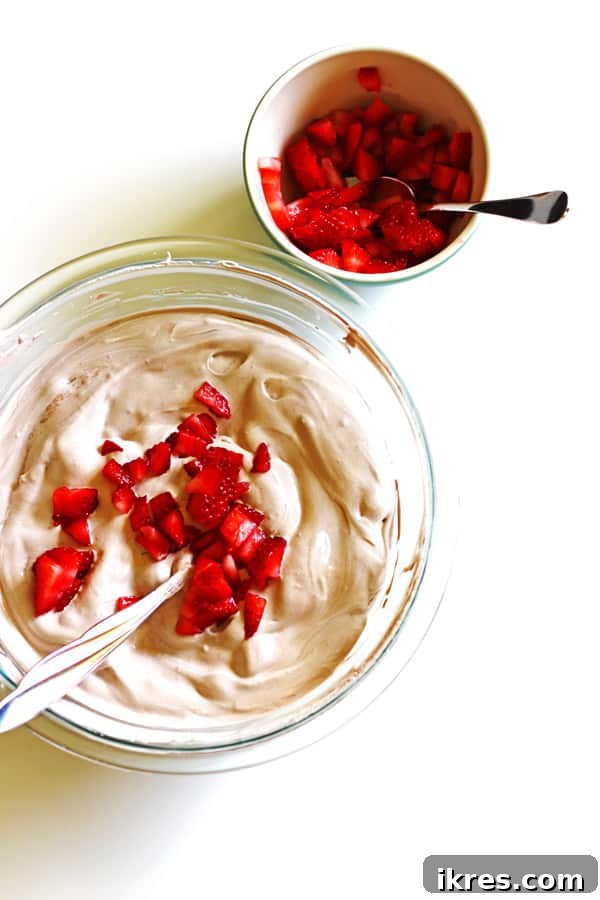 Ice Cream Pie filling in a clear pyrex bowl with diced strawberries being added to the mix