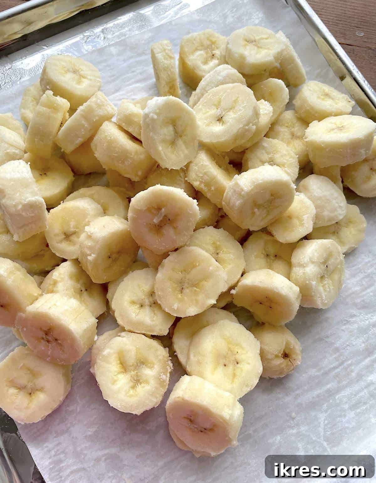 Freeze Bananas the Right Way for Smoothies 2 A pile of frozen bananas for smoothies on a parchment paper lined baking sheet.
