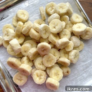 Freeze Bananas the Right Way for Smoothies 11 A pile of frozen banana slices on a parchment lined baking sheet.