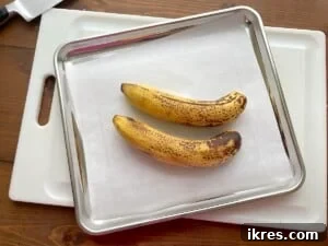 Freeze Bananas the Right Way for Smoothies 12 Two very ripe bananas on a parchment paper lined baking sheet.