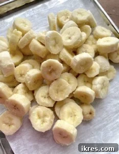 Freeze Bananas the Right Way for Smoothies 14 A pile of frozen bananas for smoothies on a parchment paper lined baking sheet.