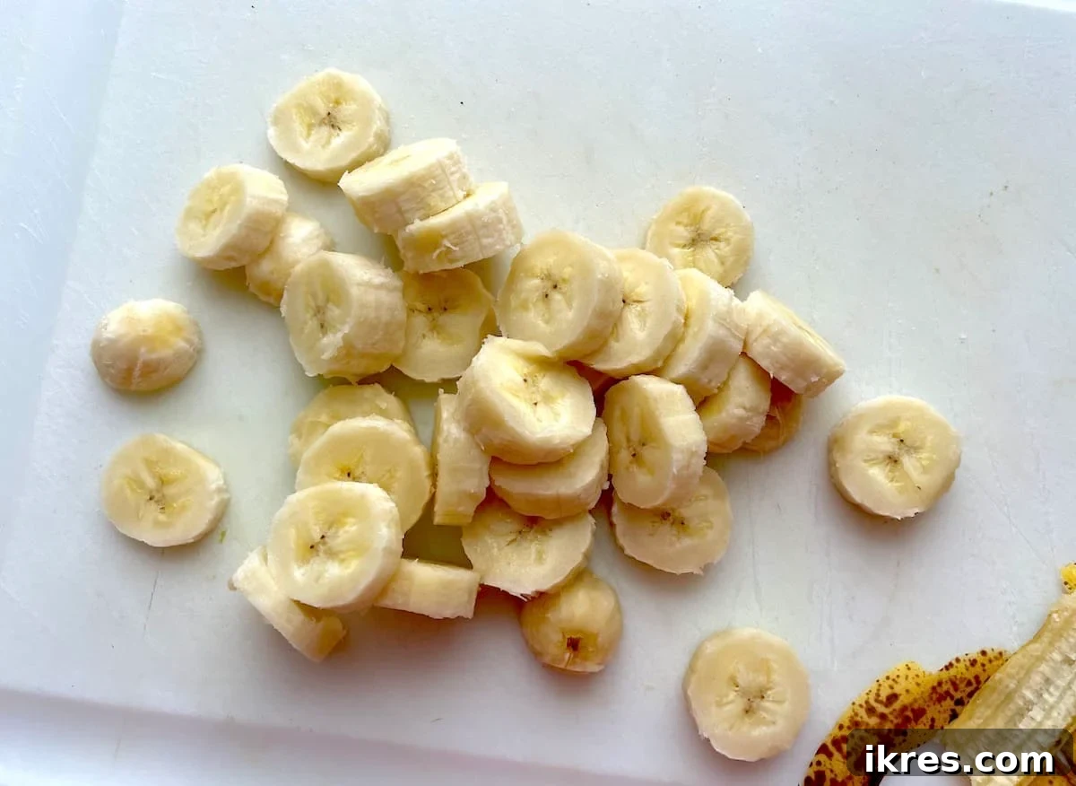 Freeze Bananas the Right Way for Smoothies 5 Sliced bananas on a white cutting board, ready to be frozen for smoothies.