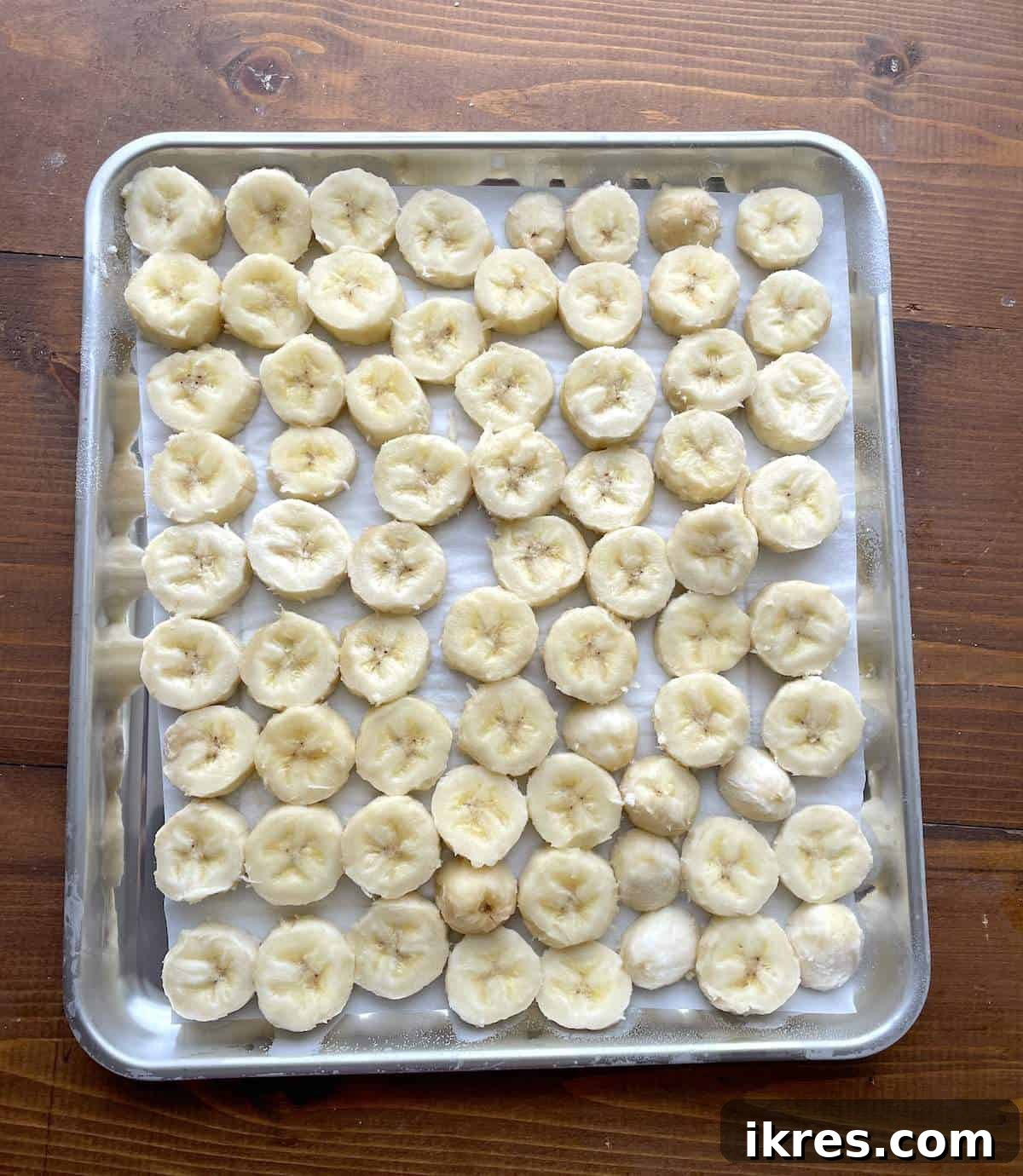 Freeze Bananas the Right Way for Smoothies 6 Bananas slices frozen in a single layer on a parchment paper lined baking sheet.