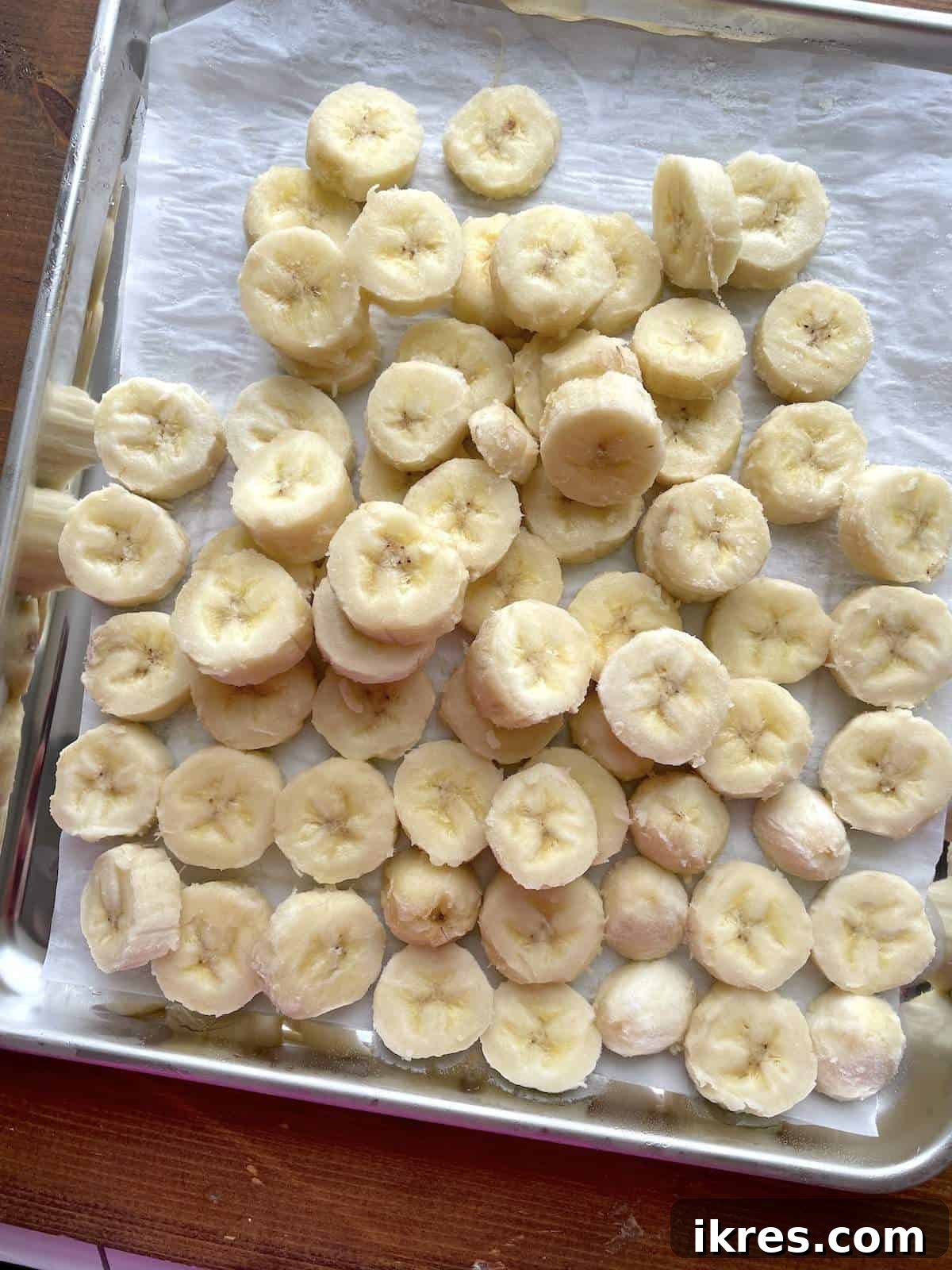 Freeze Bananas the Right Way for Smoothies 9 Slices of frozen bananas on a parchment paper lined baking sheet.