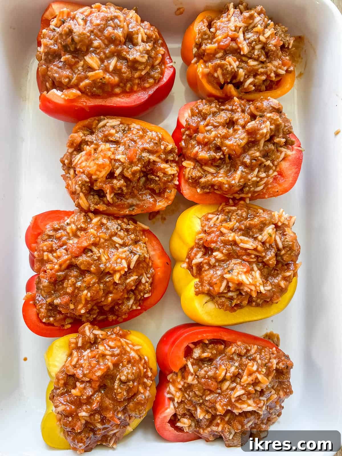 Bell pepper halves generously stuffed with the meat and rice mixture, ready for baking.