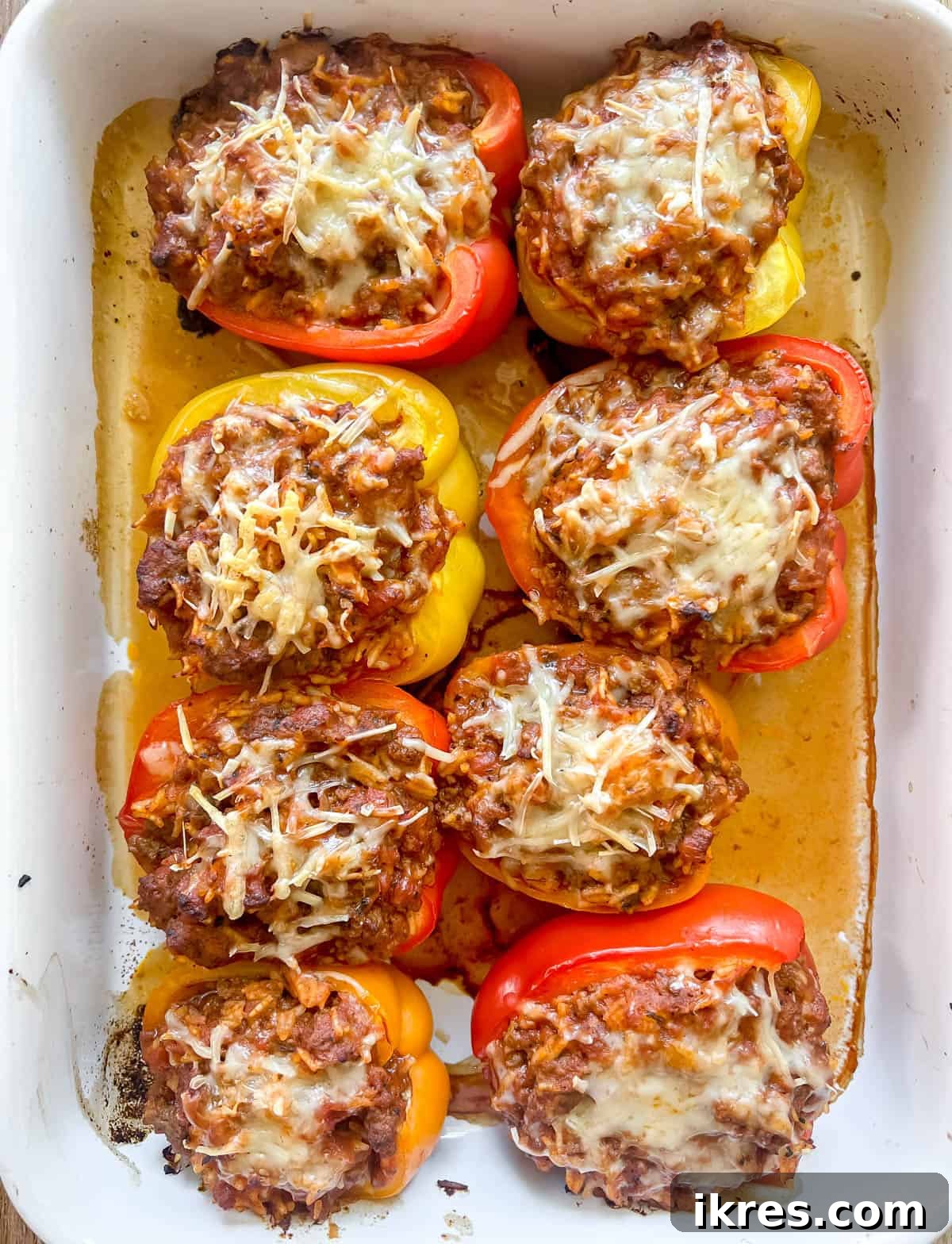 Baked stuffed peppers with ground beef and rice in a baking dish, with melted cheese.
