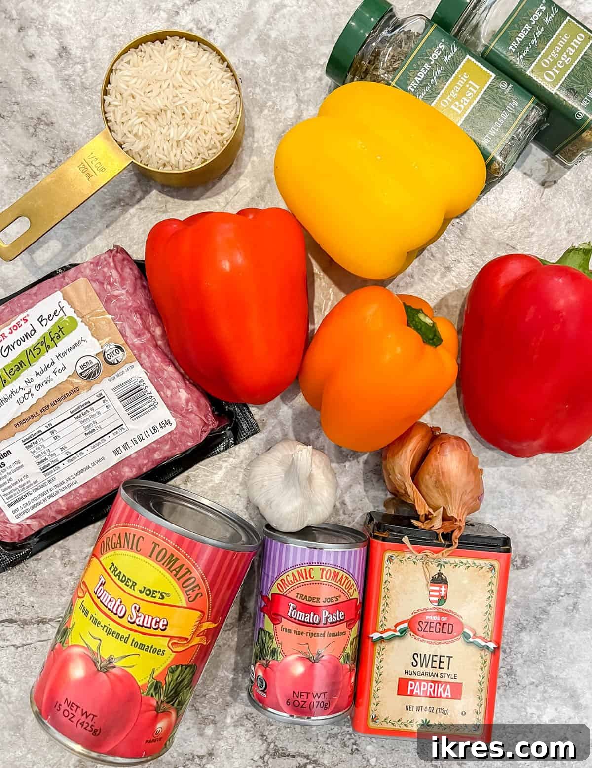 All ingredients laid out on a table for making healthy stuffed peppers: bell peppers, garlic, shallot, ground beef, herbs, tomato paste, marinara, rice, and Parmesan cheese.