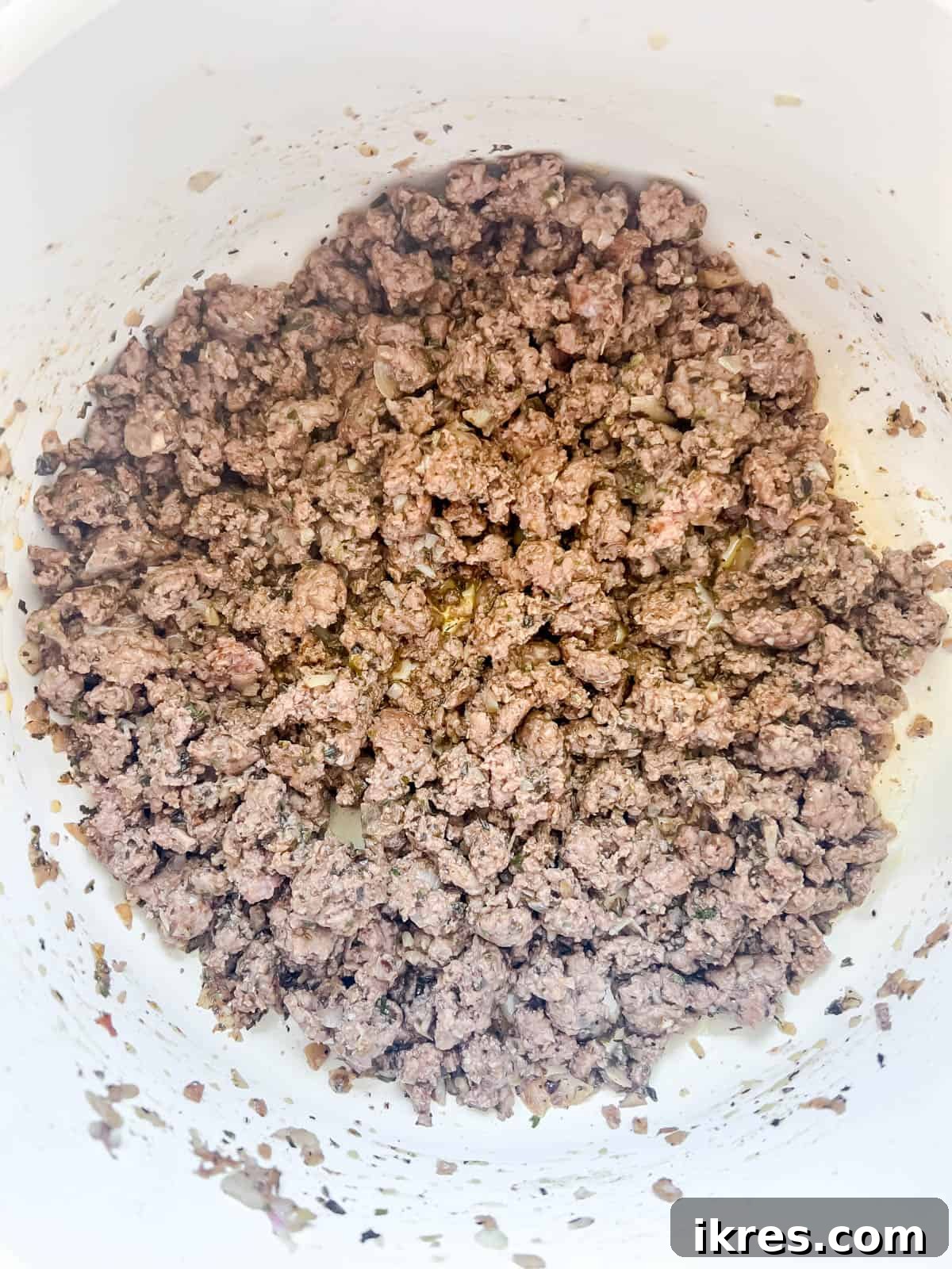 Ground beef browning in a pan with sautéed aromatics and seasonings.