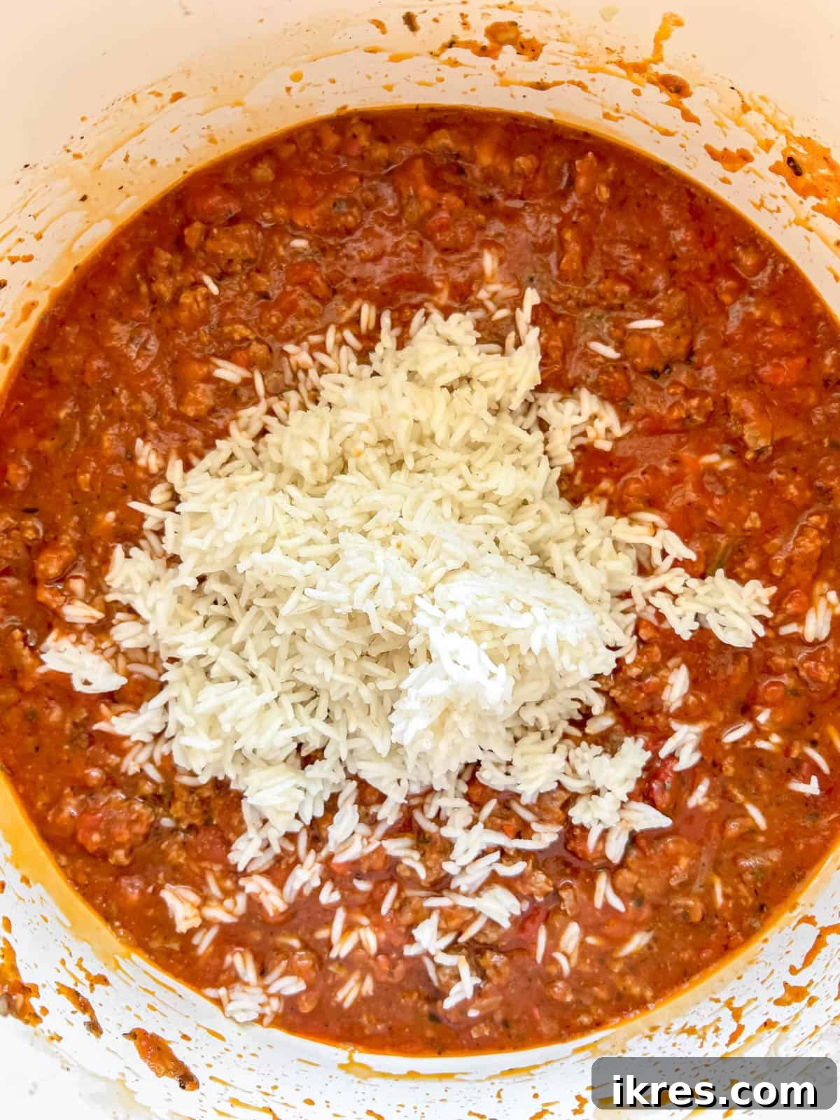 Cooked white rice being mixed into the ground beef and marinara sauce filling in a pan.