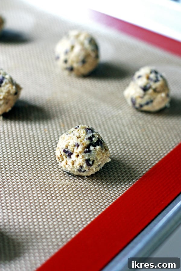 Unbaked oatmeal chocolate chip cookie dough balls placed on a silicone baking mat, ready for the oven.