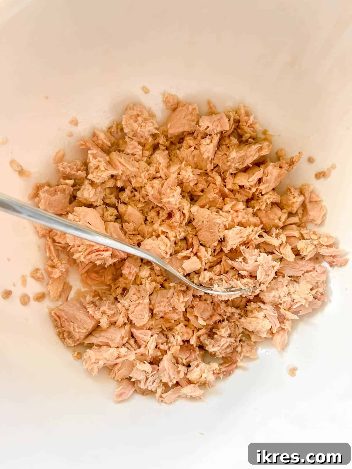 Rustic French Tuna Potato Salad 5 Canned tuna fish in a mixing bowl, being flaked into smaller, manageable pieces with a fork.