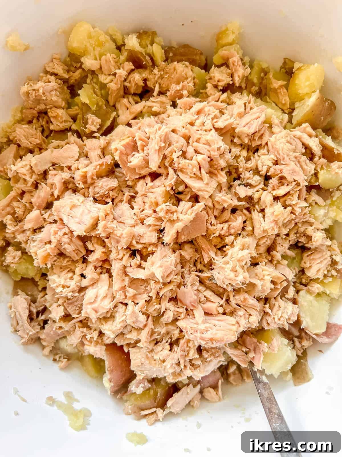 Rustic French Tuna Potato Salad 7 Flaked tuna is added on top of the cooked, diced potatoes in a large mixing bowl, ready to be combined.