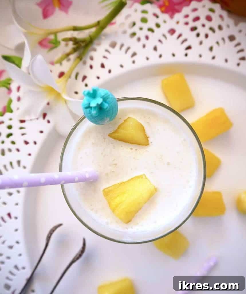 Close-up of a frothy, white Piña Colada with fresh pineapple and cherry garnishes.