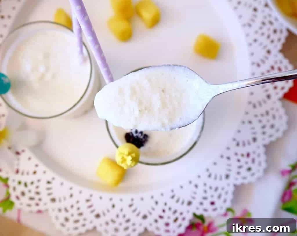 Two glasses of Piña Colada, one with a straw and pineapple wedge, on a table with fresh fruit.