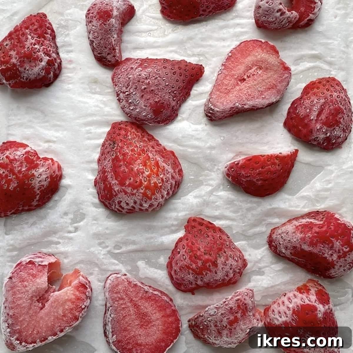 Thinly sliced frozen strawberries on a piece of parchment paper.