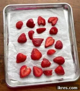 Sliced strawberries spread on a tray covered in parchment for freezing for smoothies.