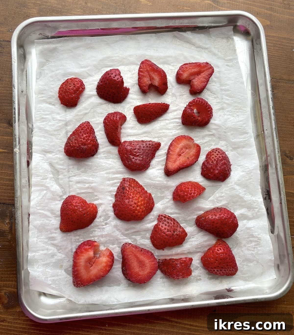 Sliced strawberries spread on a tray covered in parchment for freezing for smoothies.