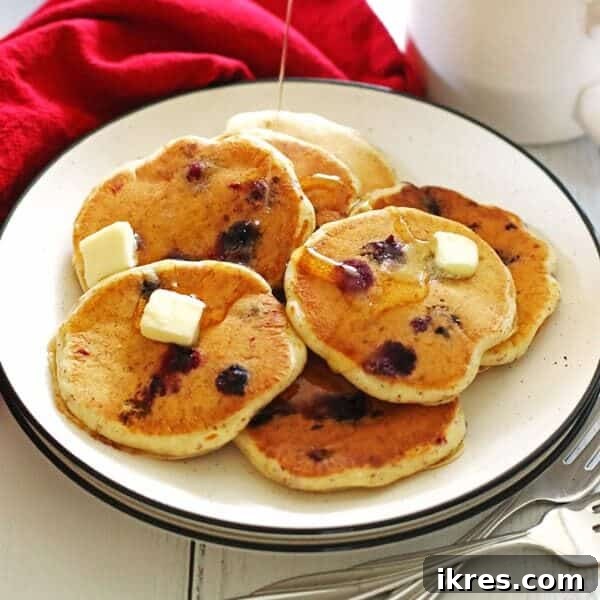 The Art of Freezing Blueberries for Smoothies and Baked Treats 9 Pancakes made with blueberries on a white plate with sliced butter on top of them and syrup being poured over them