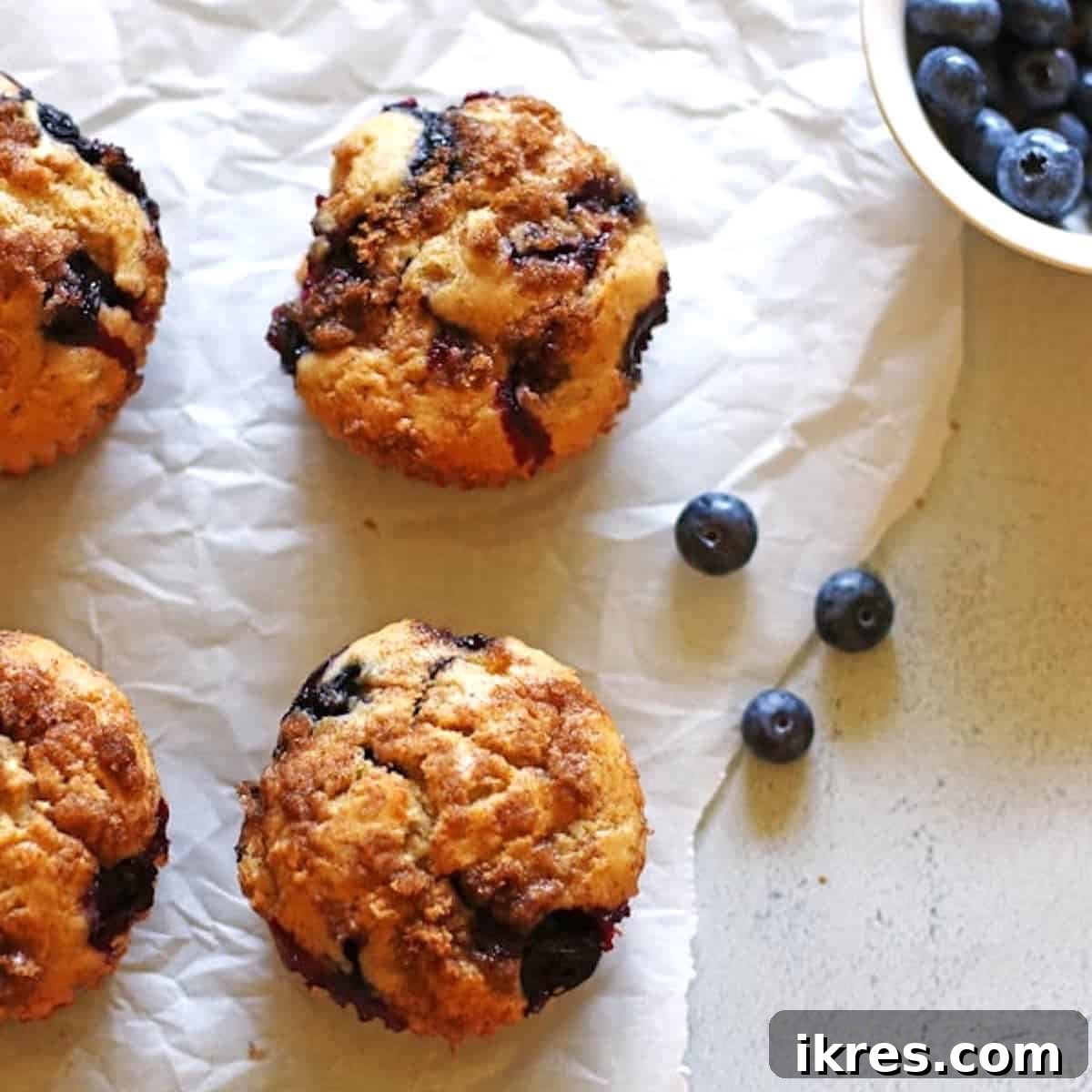 The Art of Freezing Blueberries for Smoothies and Baked Treats 10 Blueberry Banana Muffins on white parchment paper with a small bowl of blueberries next to them.