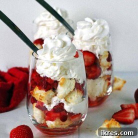 Two angel food cake strawberry shortcakes in stemless wine glasses topped with whipped cream.