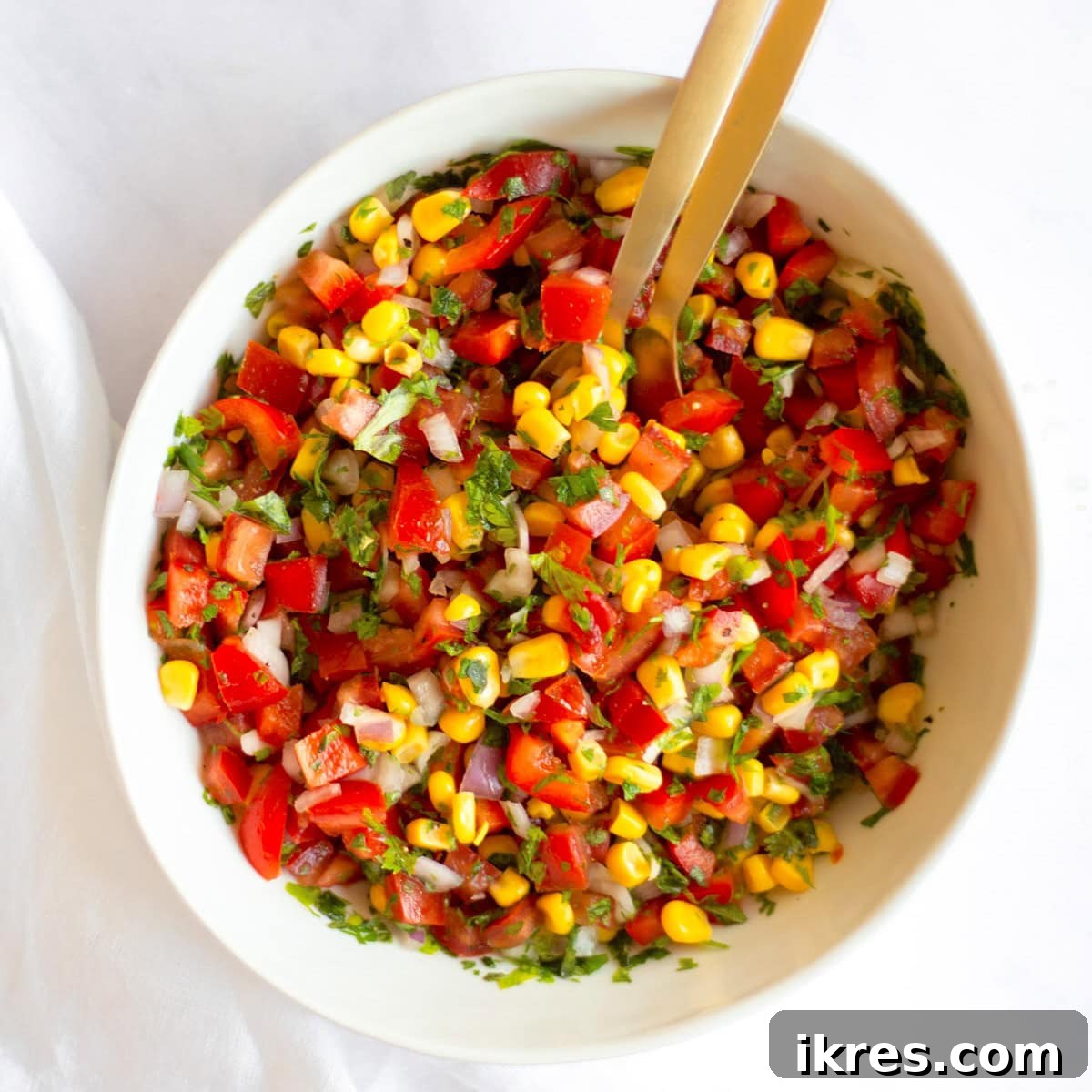 Zesty Sweet Corn Pico de Gallo 2 A vibrant bowl of Sweet Corn Pico de Gallo, perfectly mixed, with two elegant gold serving spoons resting inside.