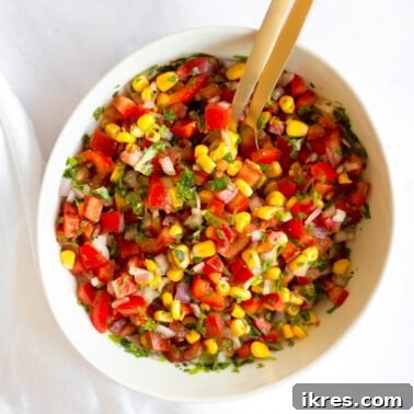 Zesty Sweet Corn Pico de Gallo 7 A vibrant bowl of Sweet Corn Pico de Gallo, perfectly mixed, with two elegant gold serving spoons resting inside.