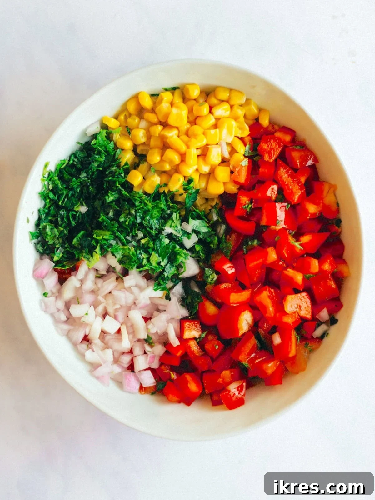 Zesty Sweet Corn Pico de Gallo 4 A large mixing bowl containing all the fresh, diced ingredients for corn salsa: vibrant peppers, sweet red onion, golden corn kernels, aromatic cilantro, and juicy tomatoes, ready to be mixed.