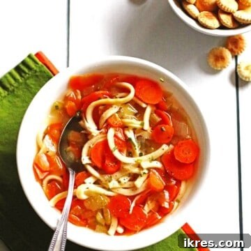 A white bowl filled with chicken soup and a spoon in it.