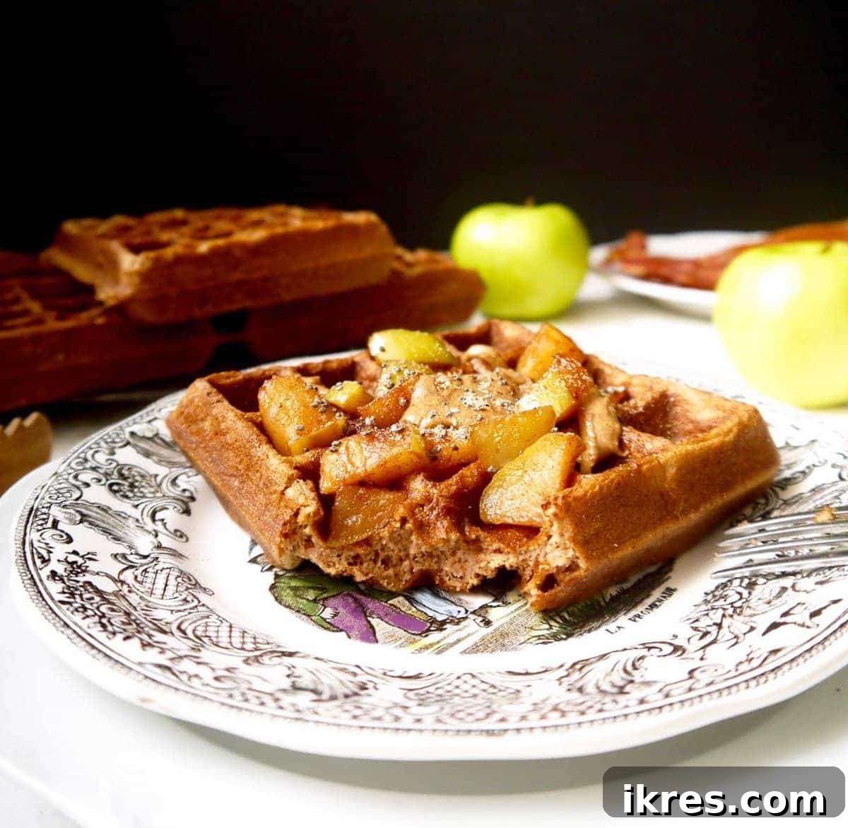 Paleo Gluten-Free Apple Cinnamon Waffles 3 Gluten-free apple cinnamon waffles on a white plate with a fork taking a bite, showing the fluffy interior.