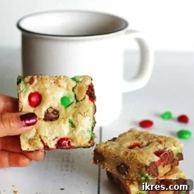 Festive Cookie Bars adorned with red and green candies, set on a table next to a white mug.
