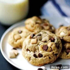 Several S'mores Cookies on a white plate with a glass of milk next to them, looking incredibly gooey and delicious.