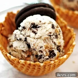 A vibrant waffle bowl overflowing with No-Churn Cookie Monster Ice Cream, featuring blue ice cream and chunks of cookies.