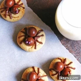 Delicious peanut butter cookies creatively decorated with candy spiders on top, placed next to a glass of milk.