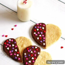 Beautiful heart-shaped Sugar Cookies, half-dipped in luscious chocolate and adorned with red, white, and pink heart sprinkles.