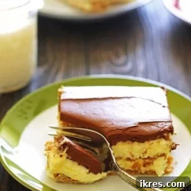 A generous slice of No-Bake Eclair Cake on a charming white and green plate, accompanied by a fork.