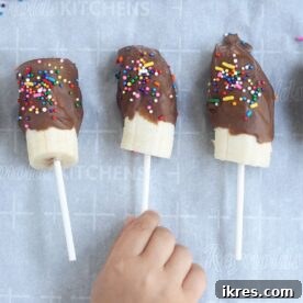 A delightful arrangement of Chocolate Covered Bananas on parchment paper, ready to be frozen into delicious pops.